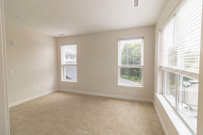 The James Apartments | Bright, spacious bedroom with beige carpet, multiple windows, and a view of the outside greenery | Luxury Apartments in Haverhill MA