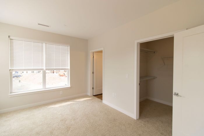 The James Apartments | Bright bedroom with beige carpet, large windows, and an open closet with wire shelving  | Luxury Apartments in Haverhill MA
