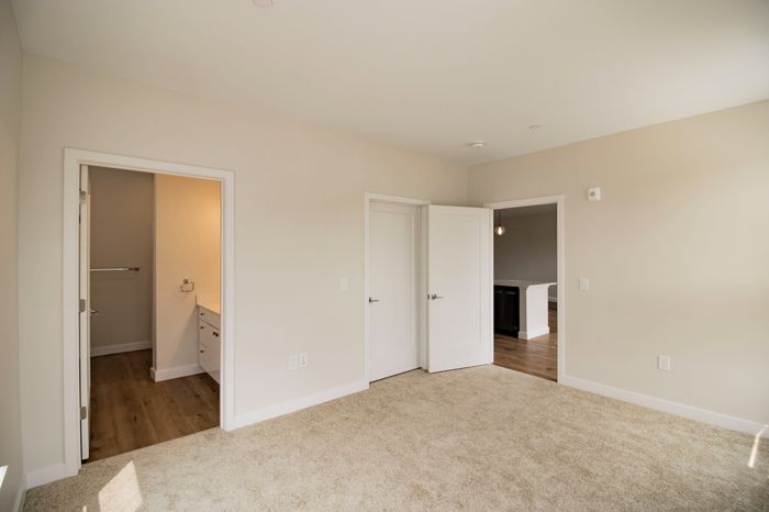 The James Apartments | Bedroom with beige carpet, multiple windows, and a door leading to a hallway with wooden flooring | Luxury Apartments in Haverhill MA