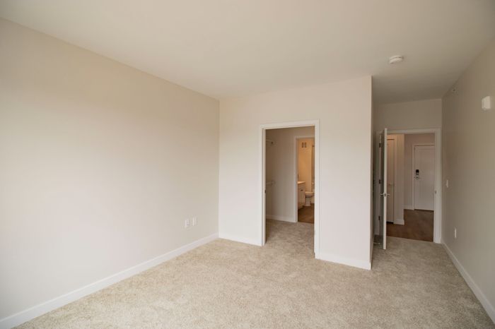 The James Apartments | Empty bedroom with carpeted floor, white walls, and a doorway leading to a walk in closet and then bathroom  | Luxury Apartments in Haverhill MA