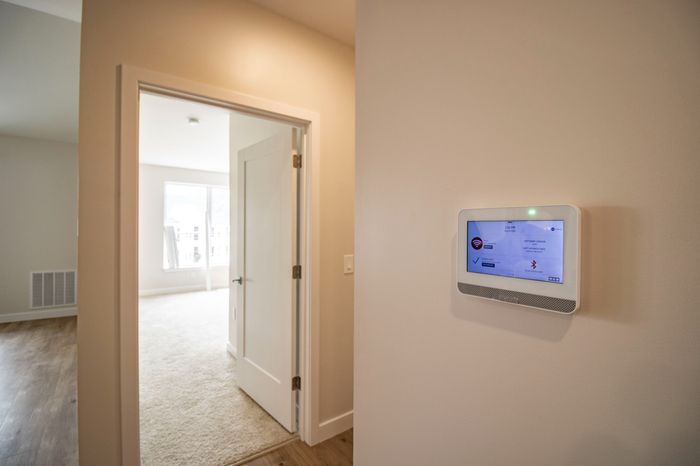 The James Apartments | Smart home ADT system panel mounted on the wall near a doorway, leading to a carpeted bedroom with natural light | Luxury Apartments in Haverhill MA