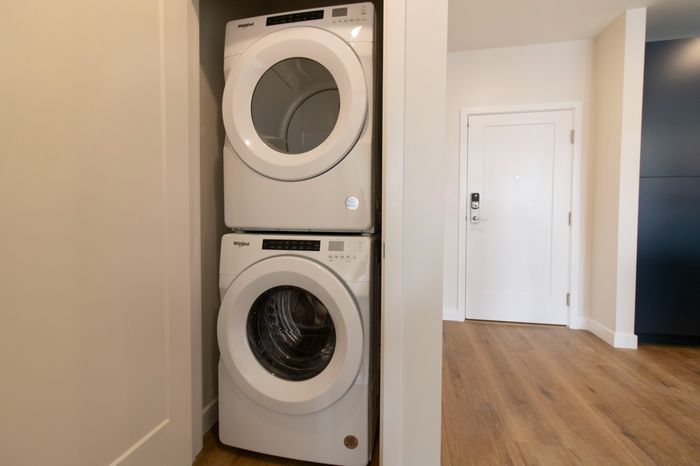 The James Apartments | Stacked white washer and dryer units in a compact laundry closet with wood-style flooring | Luxury Apartments in Haverhill MA