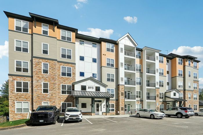 The James Apartments | Modern five-story apartment building with stone, beige, and white exterior, featuring a variety of windows and balconies. Several cars are parked in front of the building | Luxury Apartments Haverhill MA