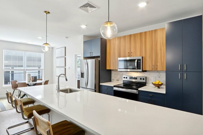 The James Apartments | Modern kitchen with a large island, pendant lighting, and bar stools, with a view of a dining area featuring large windows and a contemporary table | Luxury Apartments Haverhill MA
