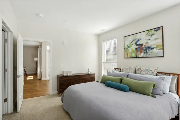 The James Apartments | Spacious bedroom with neutral tones, featuring a large bed with decorative pillows, a wooden dresser, and abstract art above the headboard | Luxury Apartments Haverhill MA