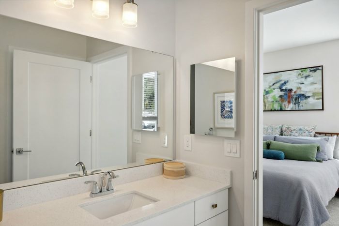 The James Apartments | Modern bathroom featuring a white vanity with a sink and mirror, with a view into the bedroom in the background, decorated with abstract wall art. | Luxury Apartments Haverhill MA