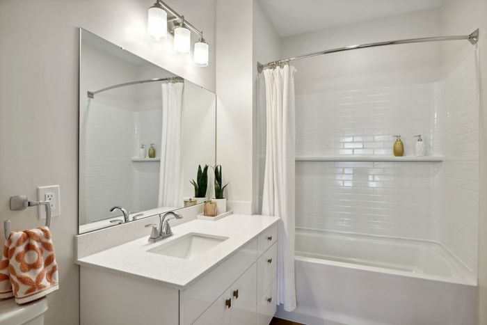 The James Apartments | Bright and clean bathroom with a white vanity, large mirror, and a bathtub with a white tiled shower and curtain. | Luxury Apartments Haverhill MA