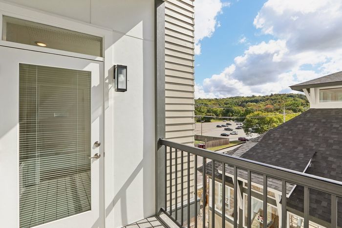 The James Apartments | Private balcony with a glass door and exterior light fixture, overlooking a parking lot and scenic tree-lined hills in the background. | Luxury Apartments Haverhill MA