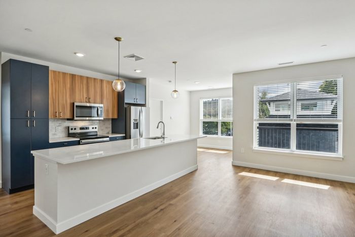 The James Apartments | Modern open-concept kitchen with an island and pendant lights, featuring stainless steel appliances and a large, unfurnished living area with hardwood floors. | Luxury Apartments Haverhill MA