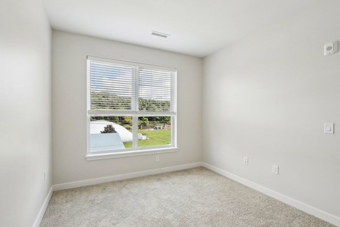 The James Apartments | Unfurnished bedroom with beige carpeting, featuring a large window that offers a view of a green outdoor area and hills. | Luxury Apartments Haverhill MA