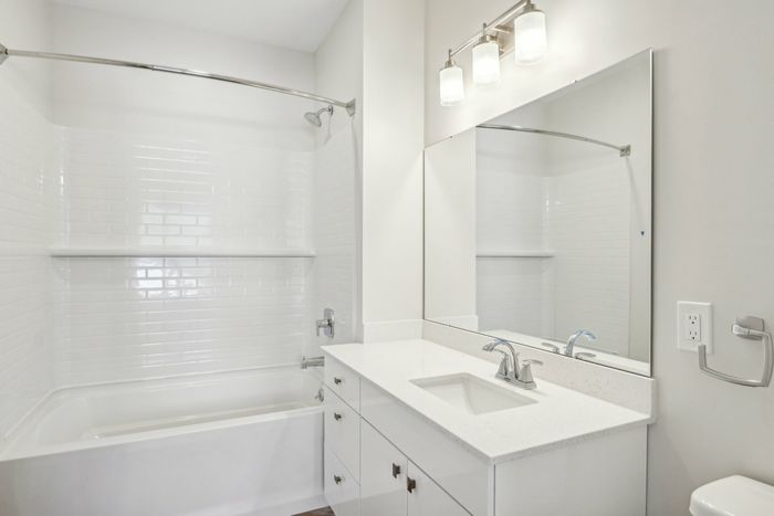 The James Apartments | Bright bathroom featuring a white vanity, large mirror, and bathtub with a white tiled shower and curtain. | Luxury Apartments Haverhill MA