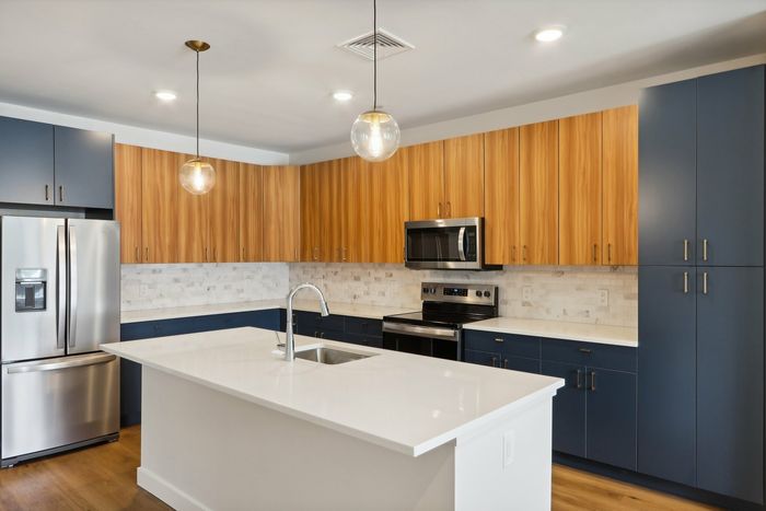 The James Apartments | Modern kitchen featuring a large island with a sink, stainless steel appliances, and a combination of wooden and blue cabinetry with pendant lighting above. | Luxury Apartments Haverhill MA