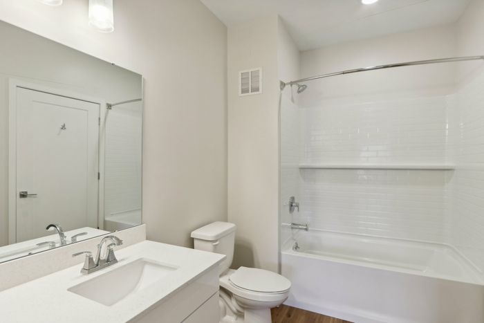 The James Apartments | Modern bathroom featuring a white vanity with a large mirror, toilet, and bathtub with a tiled shower. | Luxury Apartments Haverhill MA