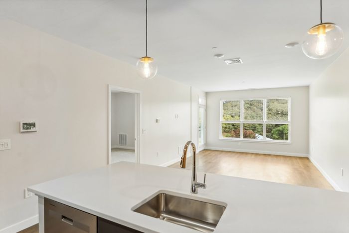 The James Apartments | View of an open living space from a kitchen island with pendant lighting, featuring large windows with a scenic view and hardwood flooring. | Luxury Apartments Haverhill MA