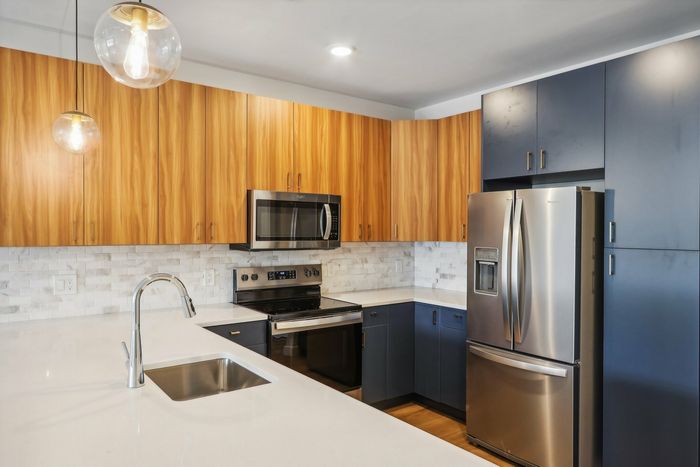 The James Apartments | Modern kitchen featuring stainless steel appliances, wooden upper cabinets, dark blue lower cabinets, and pendant lighting above a kitchen island. | Luxury Apartments Haverhill MA