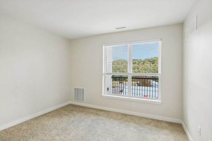 The James Apartments | Unfurnished bedroom with beige carpeting, a large window, and a view of rooftops and green hills. | Luxury Apartments Haverhill MA