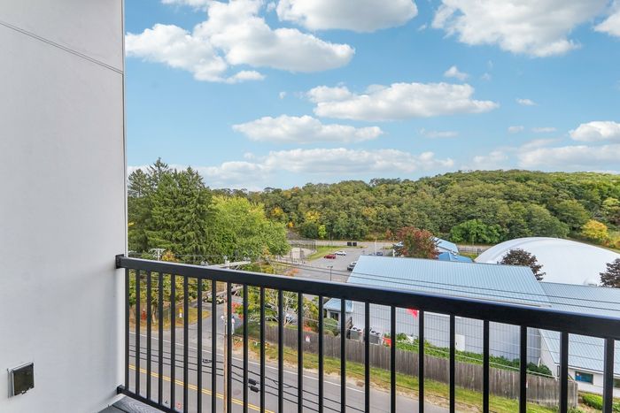 The James Apartments | Private balcony with a railing, offering a scenic view of green trees, rooftops, and a nearby sports field. | Luxury Apartments Haverhill MA