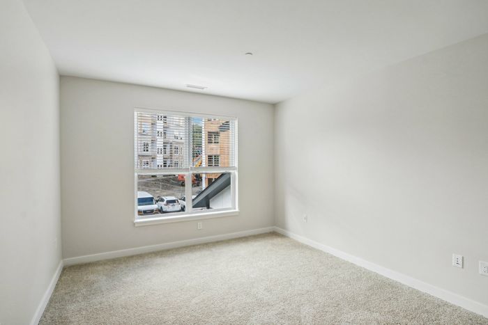 The James Apartments | Empty bedroom with beige carpet flooring and large window with views of construction outside at 895 Boston Rd. | Luxury Apartments Haverhill MA