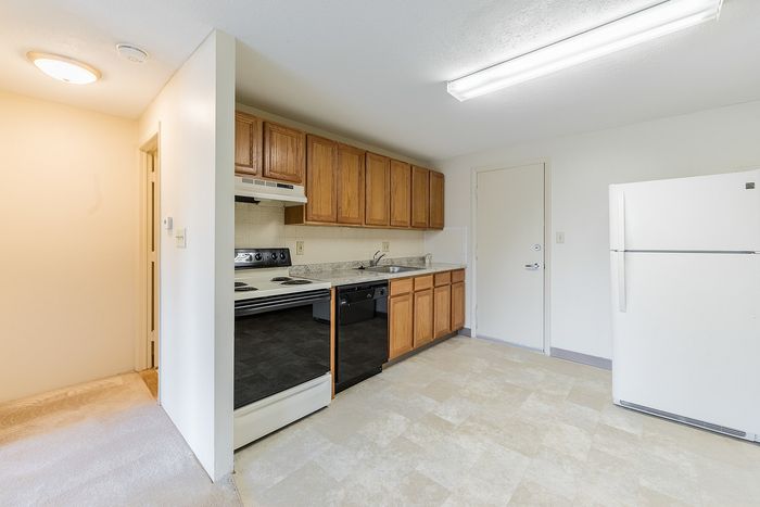 Bright and welcoming kitchen area with ample wooden cabinetry, sleek black appliances, and pristine white refrigerator.