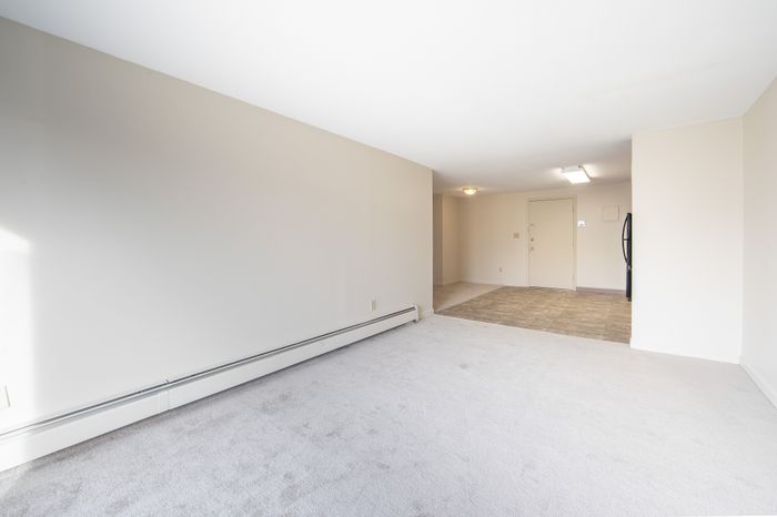 Inviting modern apartment interior with fresh carpet and bright natural light, leading to a tiled entryway with sleek contemporary lighting.