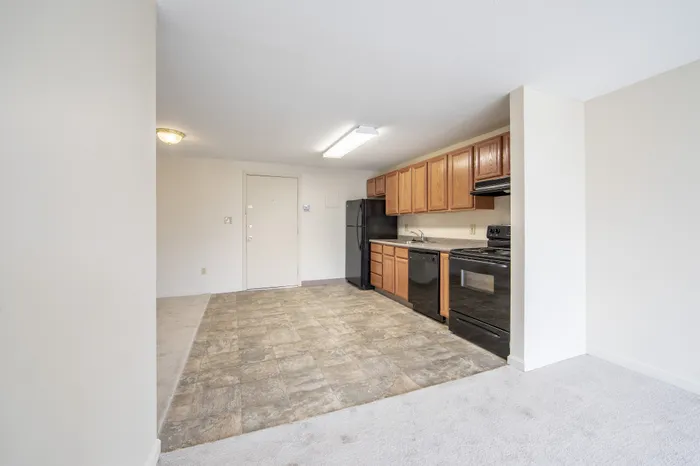 Bright, open kitchen with sleek black appliances and rich wooden cabinetry, offering a welcoming entrance to comfortable apartment living.