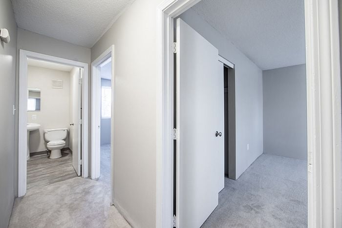 Bright and inviting hallway leading to a modern bathroom and cozy bedroom, showcasing a clean and elegant design with soft carpet and natural lighting.