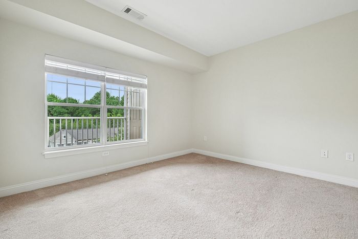 Beautiful natural light fills this spacious, carpeted room with large windows and a seamless flow into the next room at our pet-friendly apartments in Westford, MA. | Princeton Westford Apartments | Apartments with Balcony in Westford