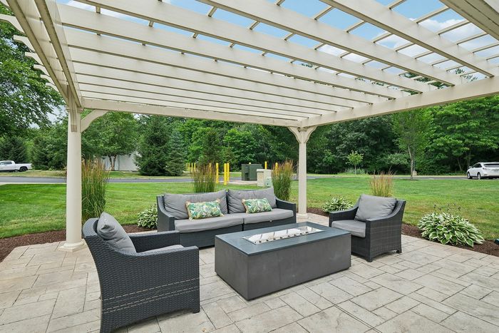 Relax outdoors in bright blue chairs under a charming pergola, steps away from the grilling area and pool at our scenic apartments in Westford, MA. | Princeton Westford Apartments | Wheelchair Accessible Apartments in Westford