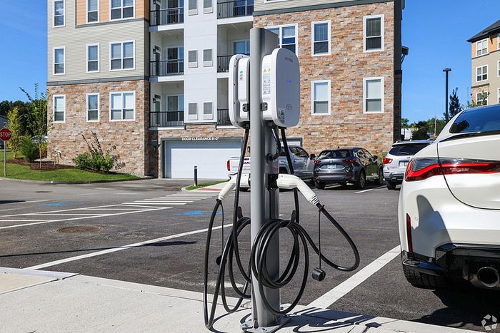 EV Charging Station with cables installed in the parking lot of The James Apartments in Haverhill, MA, with several cars parked nearby on a sunny day. The James | Apartment in Haverhill, MA