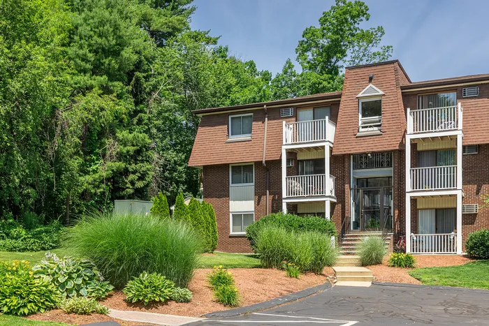 Charming brick apartment building with private balconies nestled in lush greenery, offering serene and inviting outdoor spaces.
