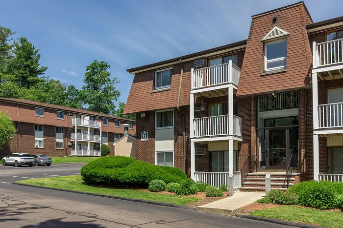 Charming brick apartment building with private balconies and lush green surroundings, perfect for serene living.