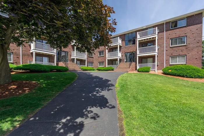 Charming brick apartment complex surrounded by lush greenery and welcoming pathways, featuring private balconies and a serene atmosphere.