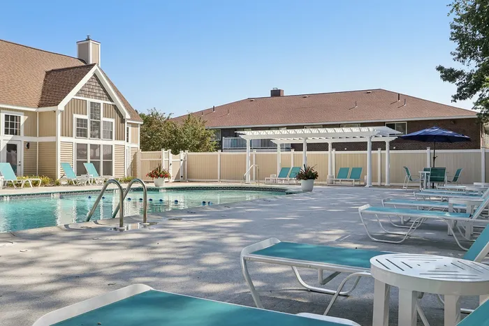 Pheasant Run Apartments | An outdoor tennis court at Pheasant Run Apartments in Nashua, NH, is surrounded by trees and a chain-link fence, with residential buildings and landscaped greenery in the background under a clear blue sky. | Apartments with Balcony in Nashua