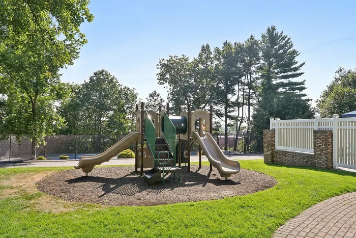Pheasant Run Apartments | Outdoor swimming pool with clear blue water, surrounded by lounge chairs and umbrellas. Apartment buildings, trees, and a white fence are visible in the background at Pheasant Run Apartments in Nashua, NH. | Apartments with Washer & Dryer in Nashua