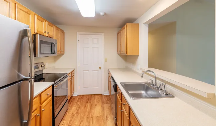 Modern kitchen with warm wood cabinetry, stainless steel appliances, and sleek countertops offers a bright and inviting cooking space.Your spacious kitchen offers generous square footage with room for multiple people and all your cooking essentials. | The Royal Crest | Apartment in,North Andover MA