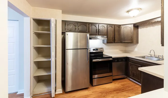 Modern kitchen with stainless steel appliances, ample wood cabinetry, and an open pantry with wooden flooring.Your spacious kitchen offers generous square footage with room for multiple people and all your cooking essentials. | The Royal Crest | Apartment in,North Andover MA