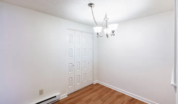 Bright dining area with elegant chandelier and stylish double closet doors, featuring modern wood flooring and white walls.Your spacious kitchen offers generous square footage with room for multiple people and all your cooking essentials. | The Royal Crest | Apartment in,North Andover MA