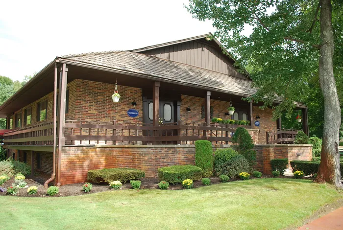 Charming brick clubhouse surrounded by lush greenery and vibrant flower beds, offering a serene and welcoming atmosphere.| The Royal Crest | Apartment in North Andover, MA