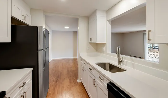 Modern kitchen with sleek white cabinets and countertops, stainless steel appliances, and elegant hardwood floors opening to a bright living area.Your spacious kitchen offers generous square footage with room for multiple people and all your cooking essentials. | The Royal Crest | Apartment in,North Andover MA