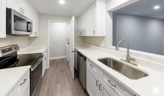 Sleek modern kitchen with stainless steel appliances, elegant white cabinetry, and chic wood-look flooring.Your spacious kitchen offers generous square footage with room for multiple people and all your cooking essentials. | The Royal Crest | Apartment in,North Andover MA