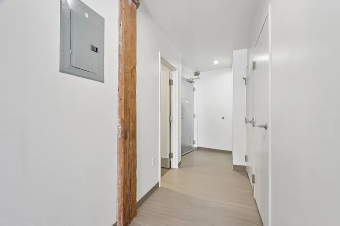 Welcome home through a beautifully designed modern hallway, showcasing sleek light wood floors and a rustic wooden beam for a chic industrial aesthetic. | 381 Congress Lofts | Apartments For Rent in Boston