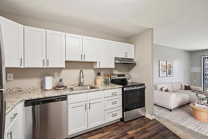 Modern kitchen with sleek white cabinets, stainless steel appliances, and cozy adjacent living area featuring a stylish sofa and elegant decor.