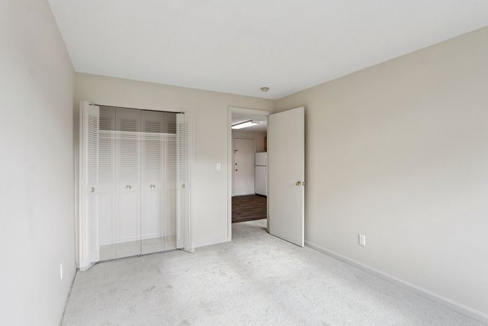 Bright and spacious bedroom with soft carpet flooring, featuring a double-door closet and an open doorway leading to the kitchen area.