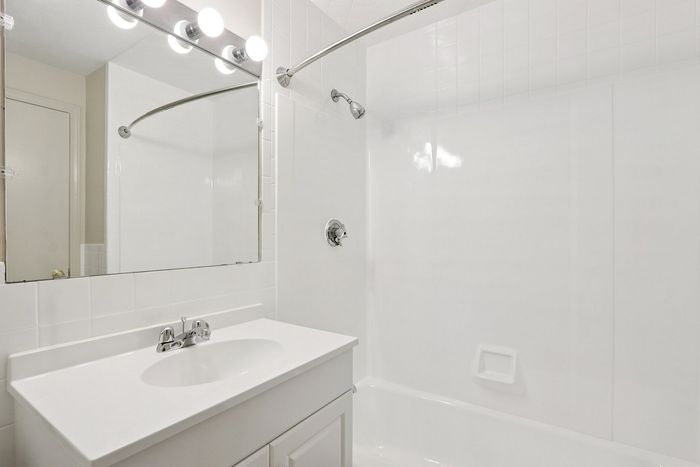 Sleek modern bathroom featuring a bright white vanity, elegant mirror, and a curved shower rod for a sophisticated touch.