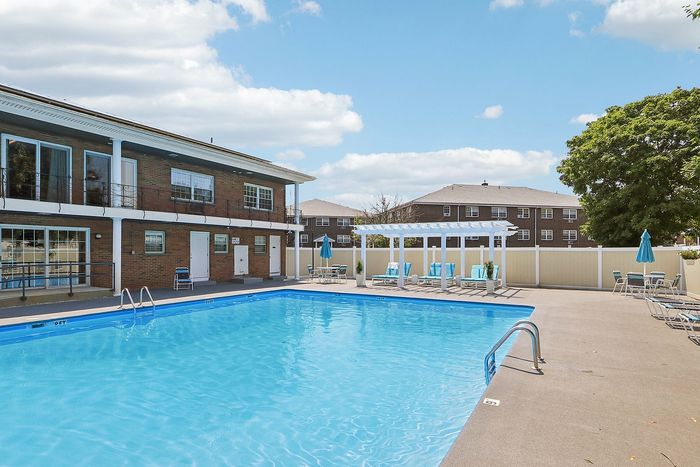 Inviting outdoor pool area with sun loungers, shaded seating, and beautiful brick buildings under a clear blue sky.