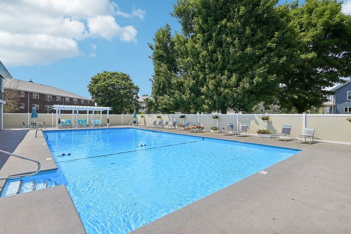 Inviting outdoor swimming pool area with sun lounges and pergola, surrounded by lush greenery, perfect for relaxation and leisure.