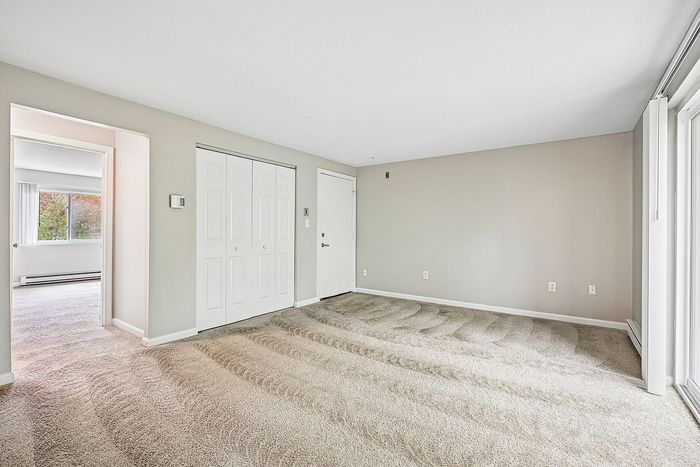 Bright, spacious room with plush carpet and ample natural light, featuring a closet and a large window offering a view.