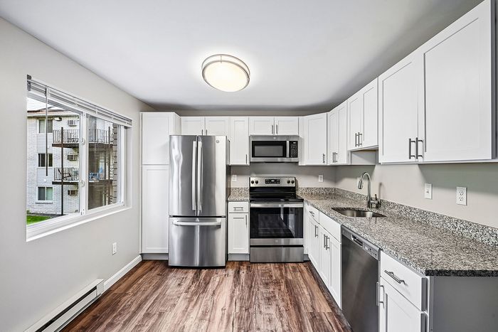 Modern kitchen with stainless steel appliances, granite countertops, and sleek white cabinetry, featuring a bright window view.