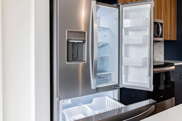 Modern stainless steel refrigerator with French doors open, showcasing spacious and well-lit interior, perfect for a contemporary kitchen.