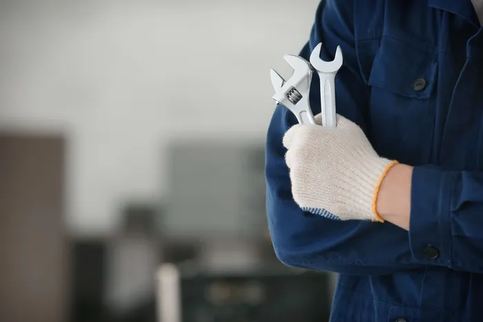 Professional repair service concept with a worker in blue uniform holding wrenches and spanner.